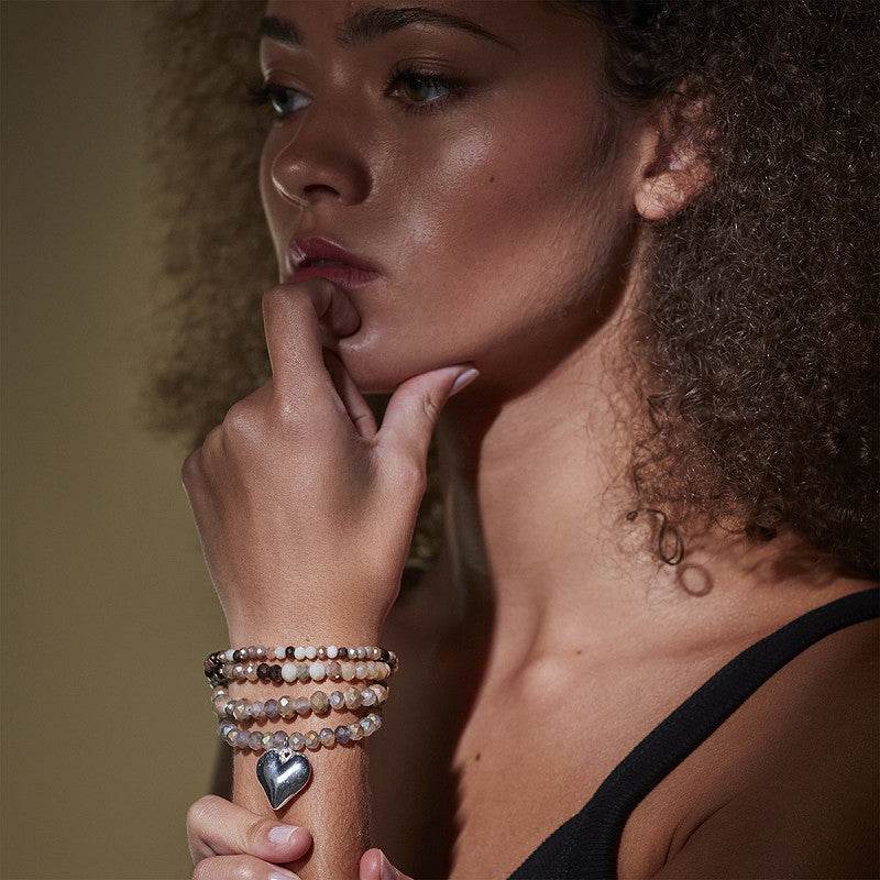 The Moshi Perlenarmband Violet mit Glasperlen in Naturtönen und Herz Anhänger silber, elastisches Boho Armband Set am Handgelenk getragen