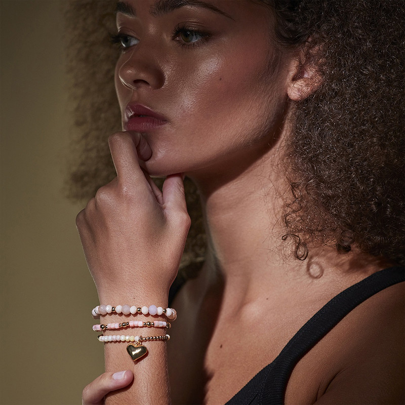 The Moshi Perlenarmband Ruby mit rosa Glasperlen und goldenem Herz Anhänger, elastisches Armband Set am Handgelenk getragen